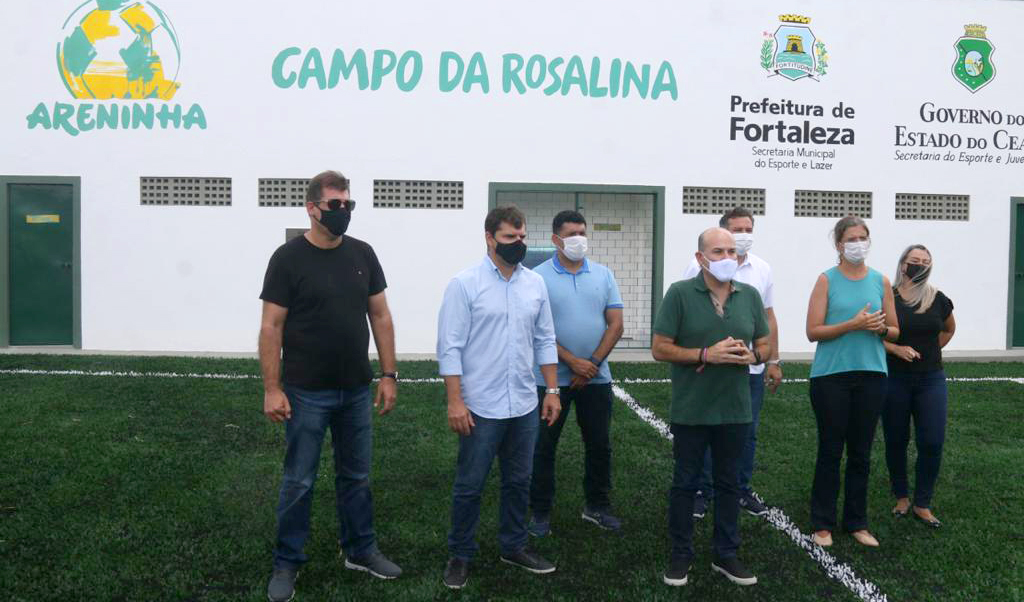 prefeito e grupo de pessoas ao lado, todos em pé com fachada da Areninha ao fundo